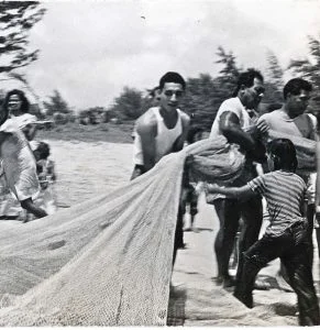 Hawaiian men pull a fishing net back to shore.