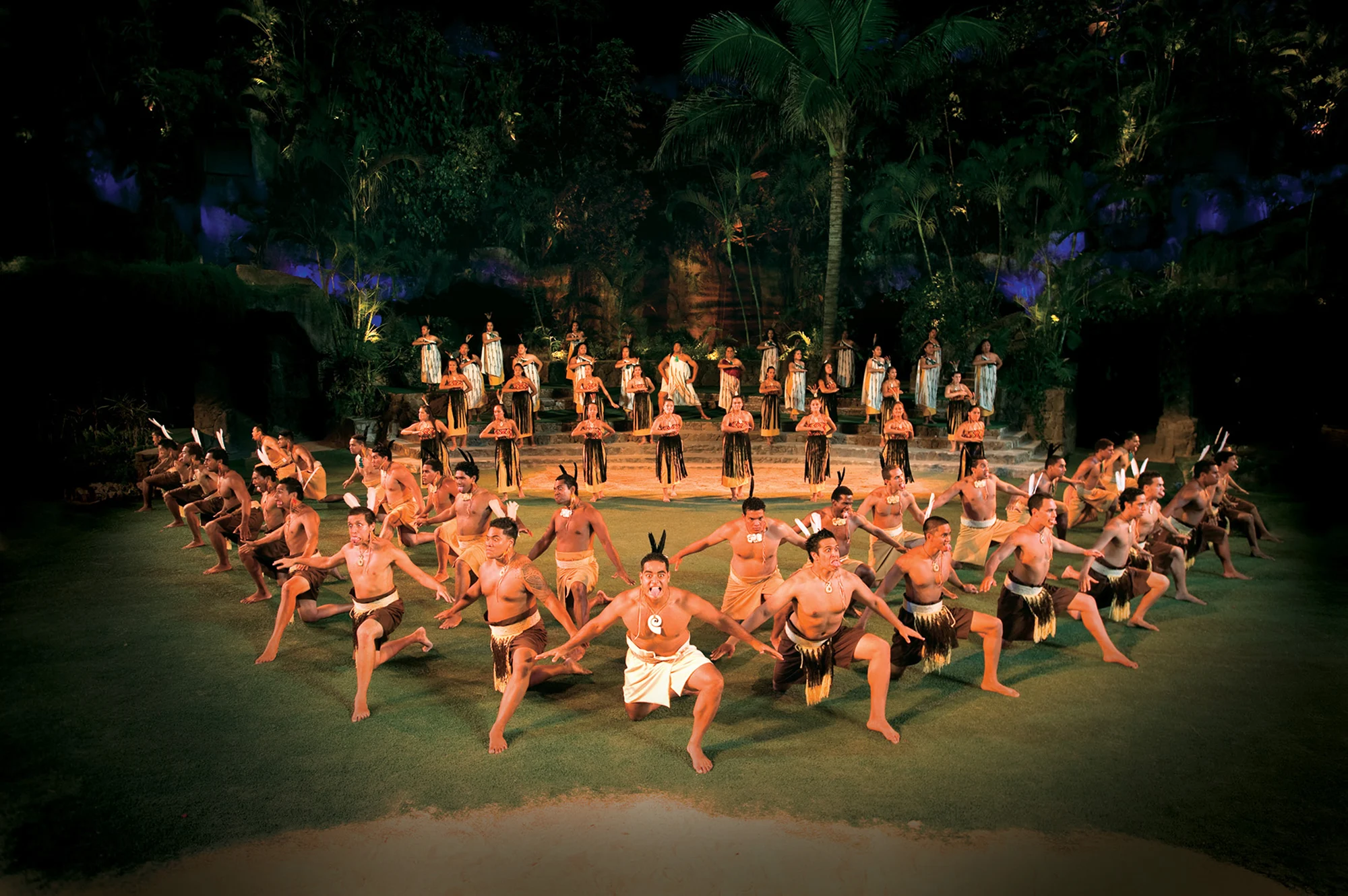 Male performers in a large group perform the haka on an outdoor stage, with a row of female performers standing behind them, during the Aotearoa segment of the HĀ: Breath of Life show at the Polynesian Cultural Center