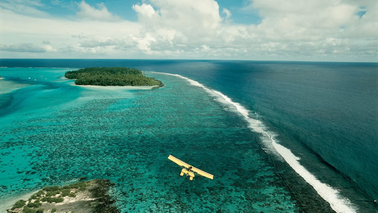 Small plane flying above waves and coral reef.