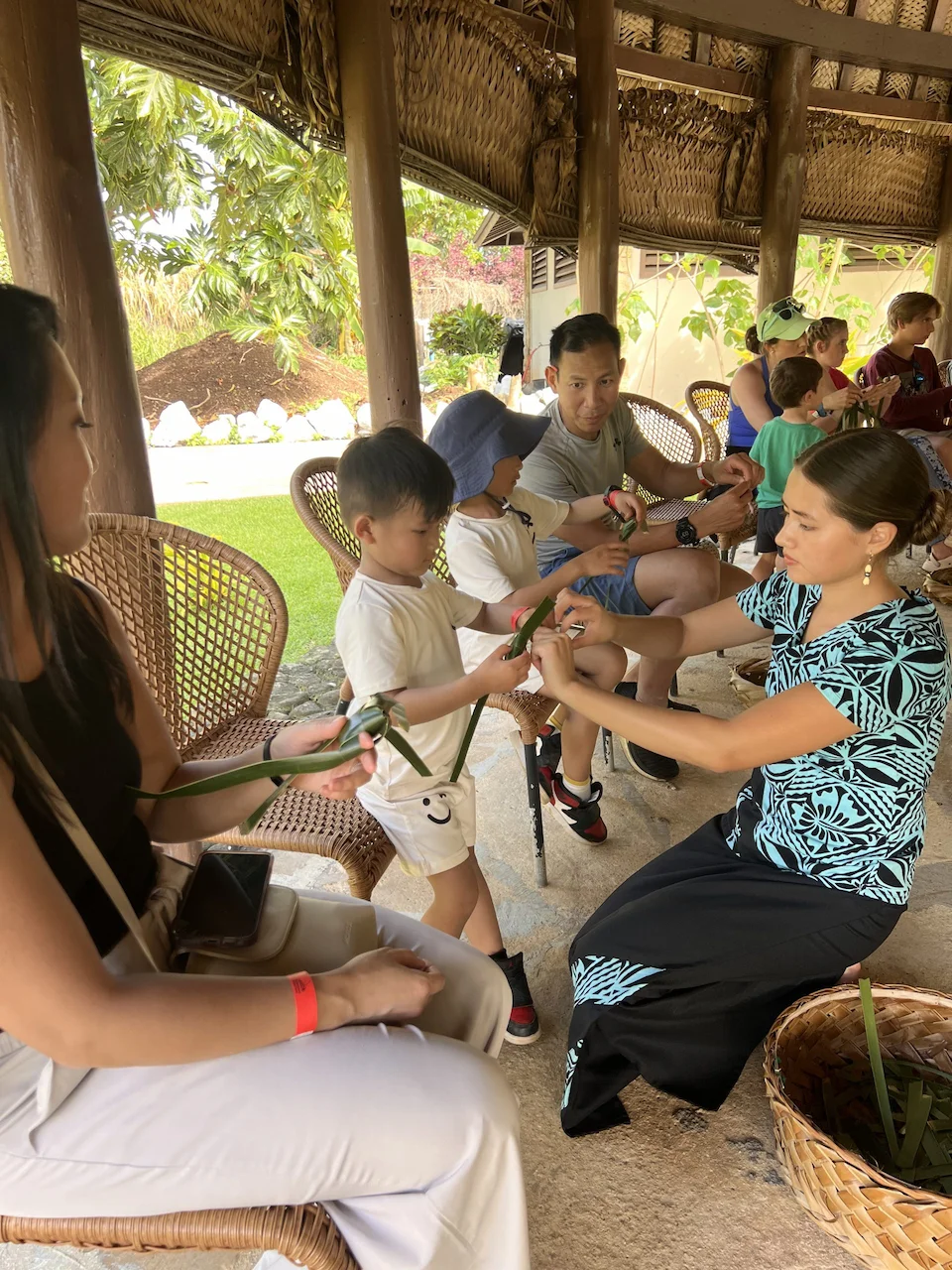 Family learns to weave fish from coconut leaves.