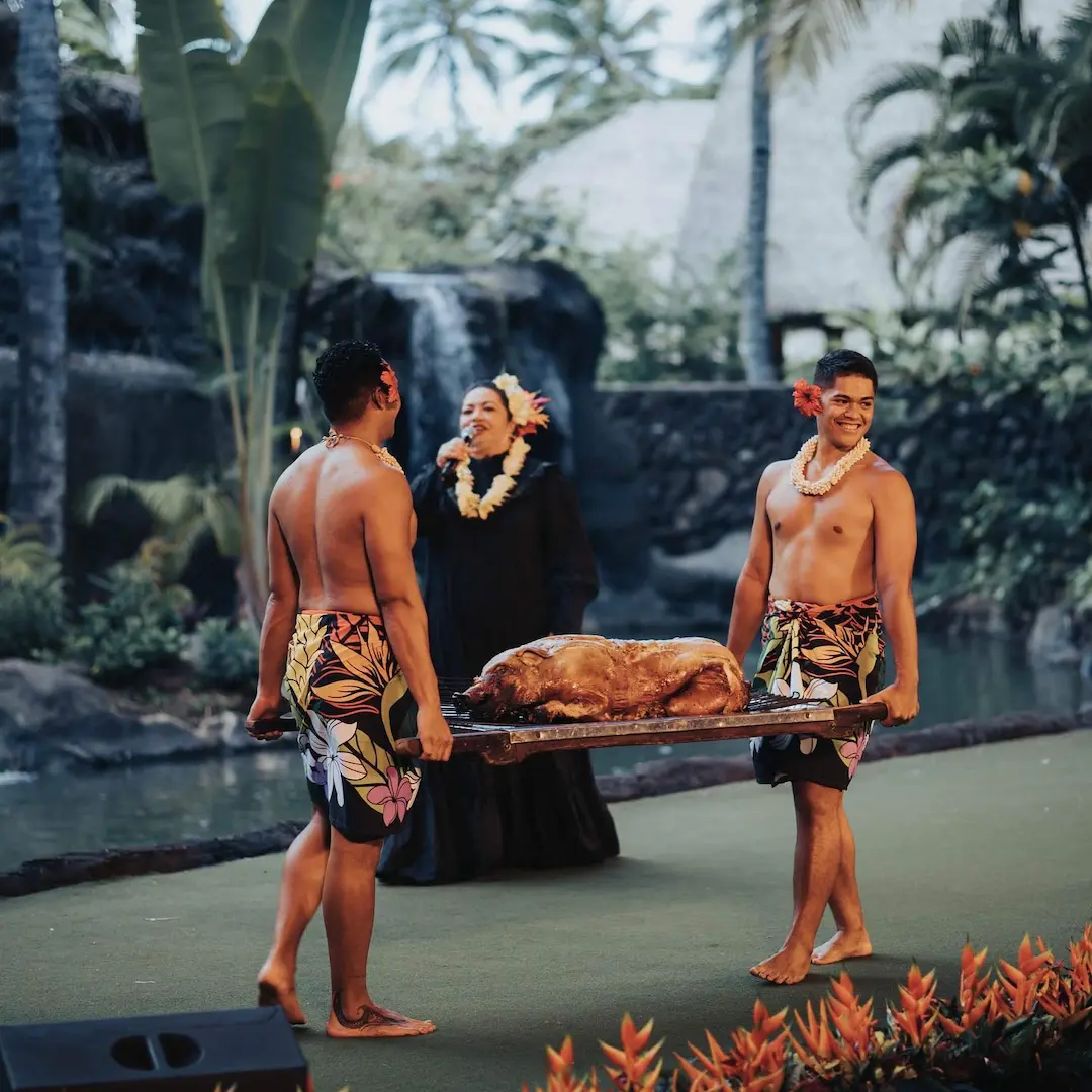 Mistress of Ceremonies and two Polynesian servers carrying a roasted pig.