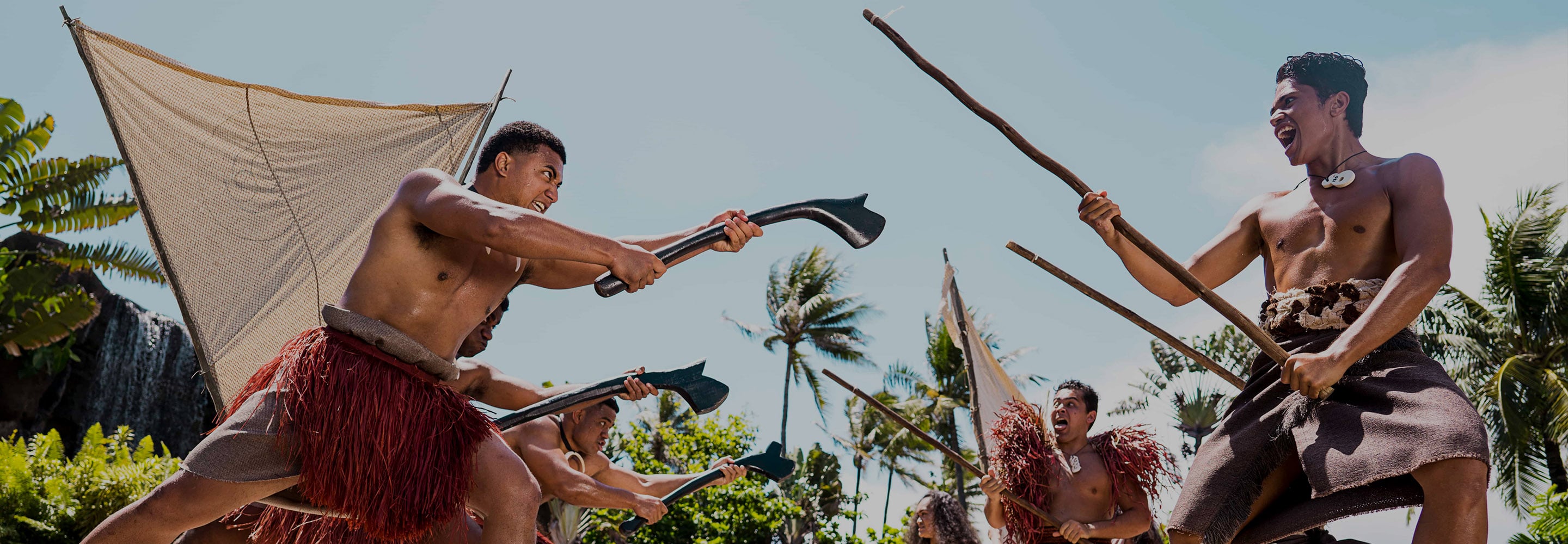 Warriors face off with paddles and spears beside a sailing canoe in Huki, the canoe show on the Polynesian Cultural Center water stage