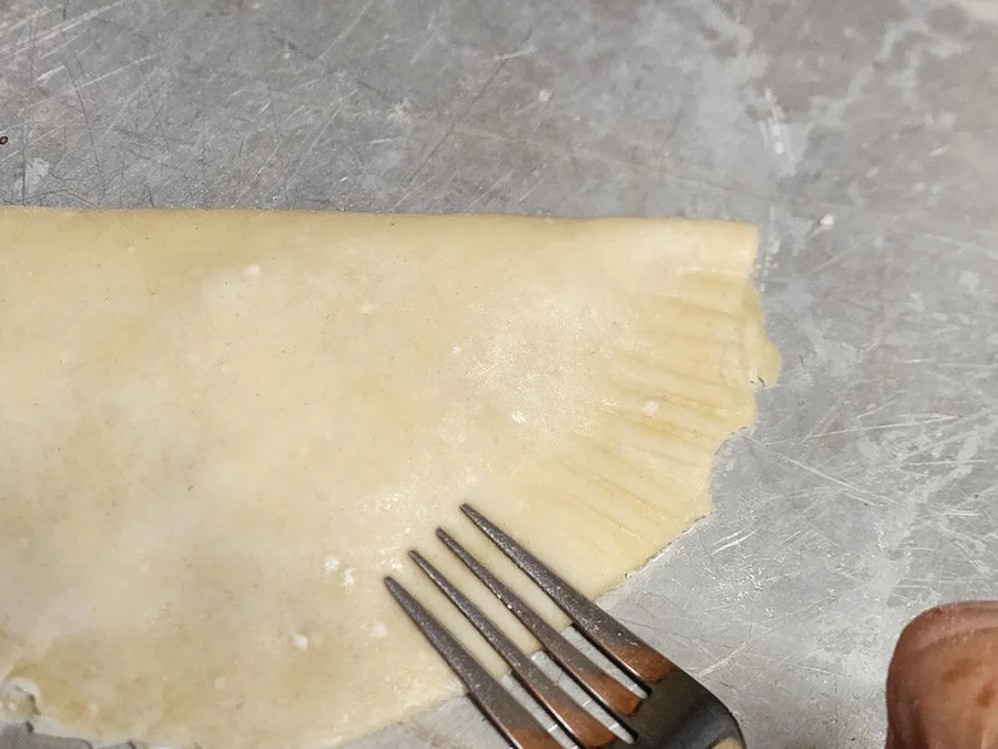 Crimping the edges of the crust by pressing with a fork.