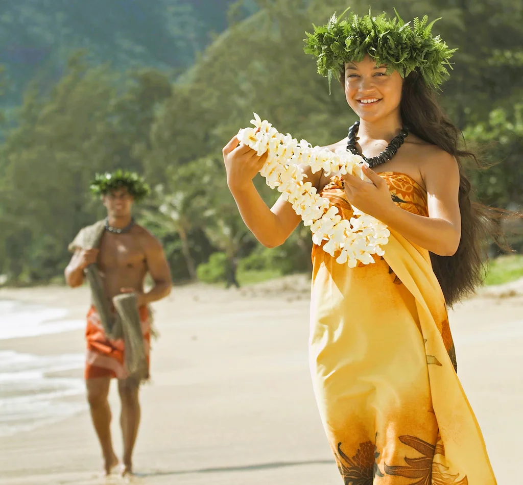A young woman and man showcases the Hawaiian word Aloha. Both wear Hawaiian attires, hakus (headpiece), kukui nuts necklaces, and traditional Hawaiian leis.