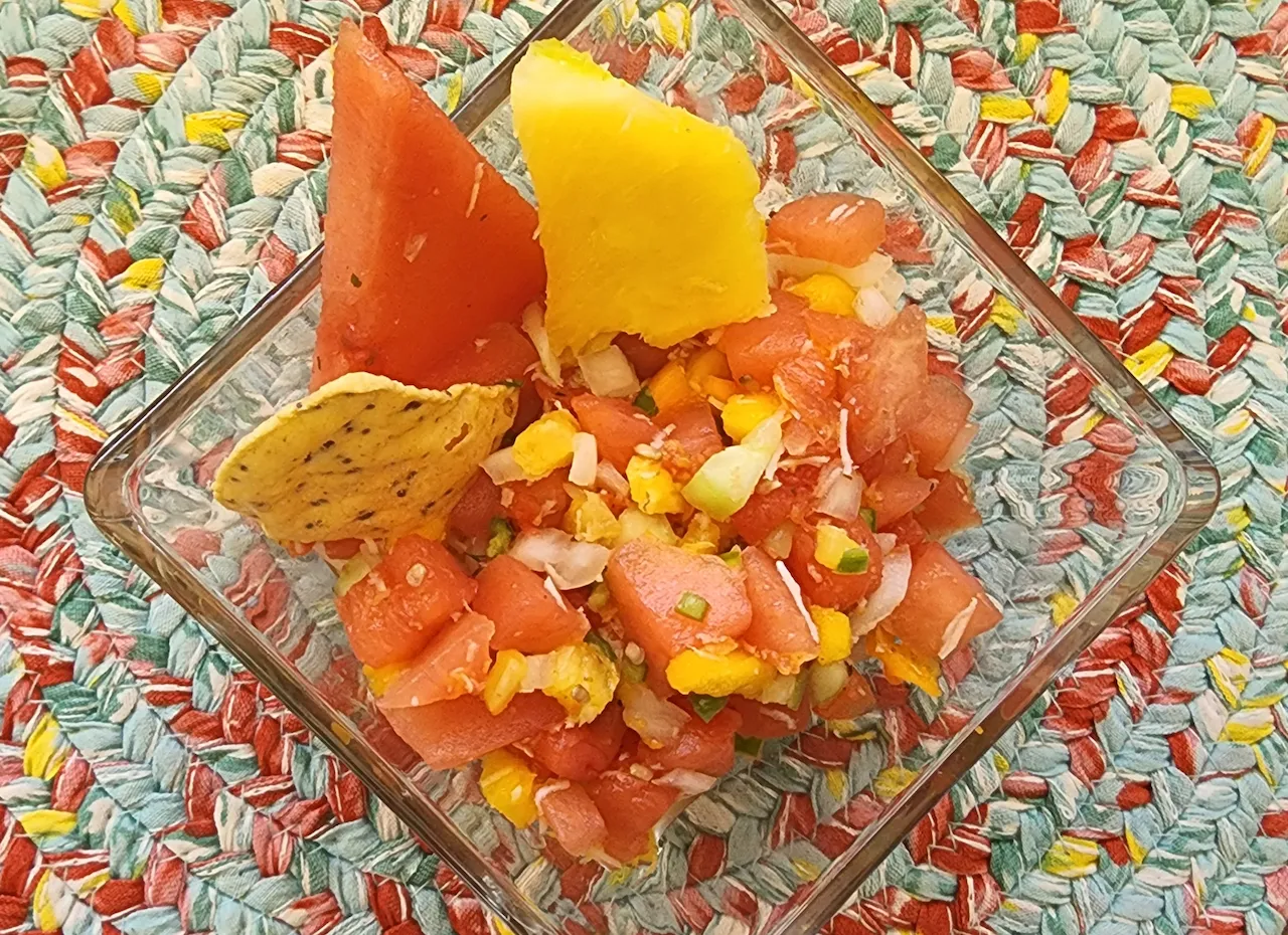 small bowl of tropical fruis salsa with a slice of pineapple, a slice of watermelon and a tortilla chip
