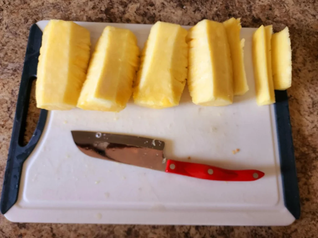 The pineapple quartered and laid on the cutting board, with the skin and core removed.