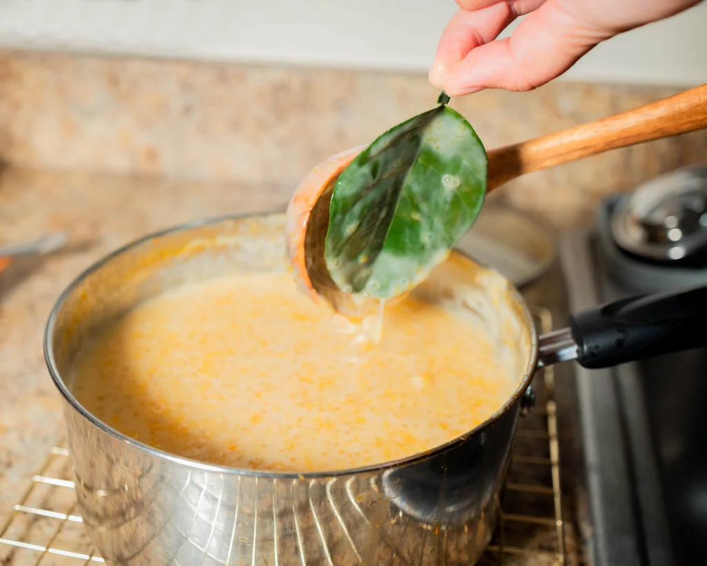 A lemon leaf being removed from the supoesi with a wooden spoon.