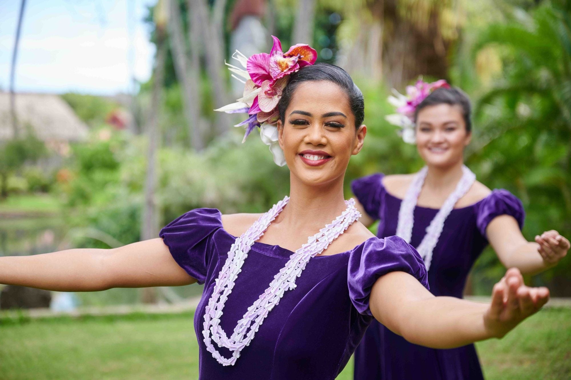 A PCC hula dancer in a purple velvet holokū and white lei