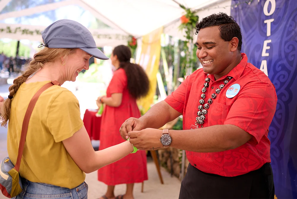 Smiling Polynesian Cultural Center host fastening an admission wristband on a guest